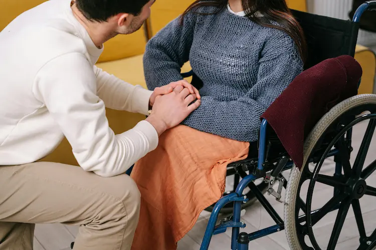 Ein Mann hält die Hand einer im Rollstuhl sitzenden Frau