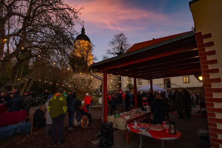 Menschen kaufen Kuchen, im Hintergrund ein Sonnenuntergang und der Turm der Kirche Ammendorf