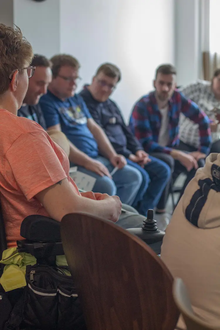 Eine Frau im Rollstuhl erklärt etwas, Menschen hören ihr zu